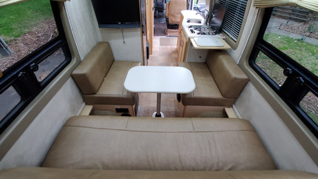Bright RV rental interior highlighting a dinette, kitchen area with sink/stove, and mounted TV. Ready for adventure!