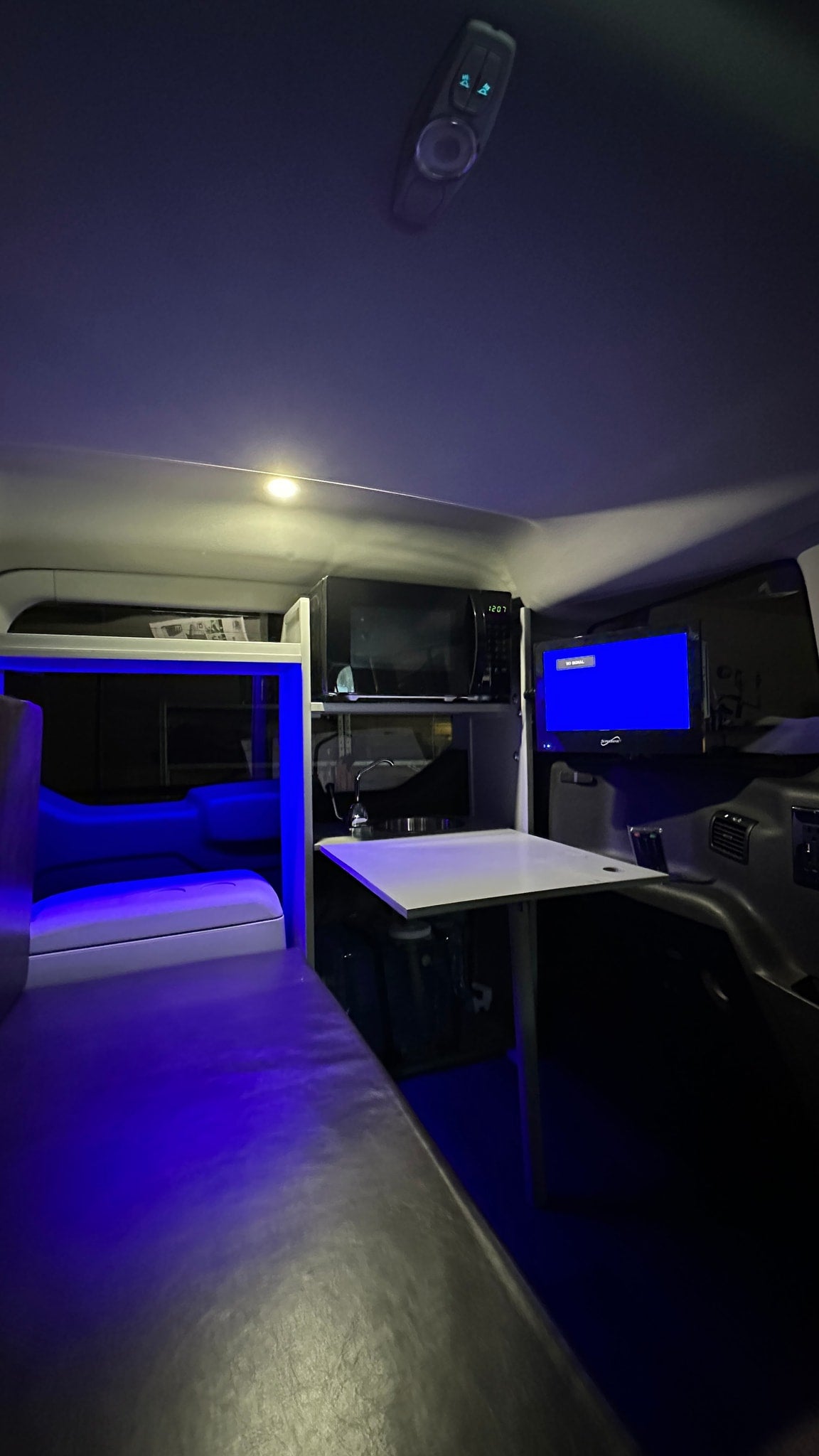 Cozy RV rental interior with blue ambient lights, a microwave, TV, and dinette setup. Perfect for mobile adventures. — photo 7