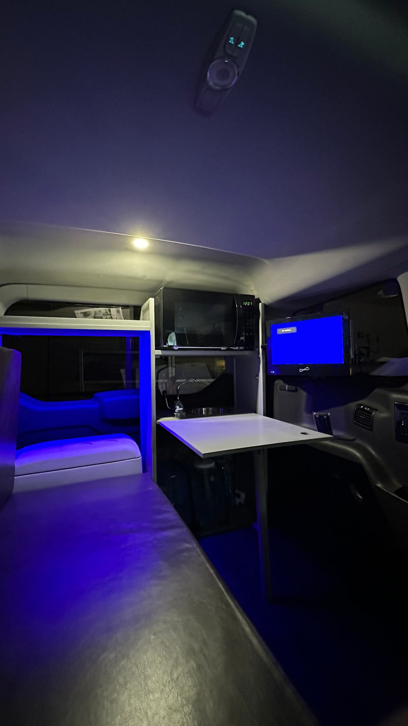 Cozy RV rental interior with blue ambient lights, a microwave, TV, and dinette setup. Perfect for mobile adventures. — photo 7