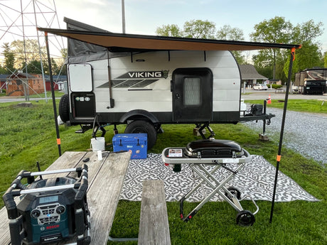 This RV rental showcases a compact Viking travel trailer with an extended awning, outdoor grill, and picnic table at a serene campground.