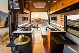 This RV rental's interior reveals a sleek kitchen, comfy seating, and amazing desert sunset views through the open rear doors.