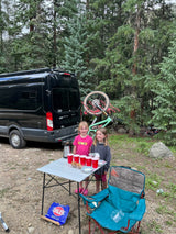 Two happy girls next to their rv rental camper van, bikes, and snacks at a forest campsite. Perfect for family adventures!