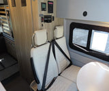 RV rental interior: two passenger seats with seatbelts, a small table, and wall-mounted controls. A window shows outside.