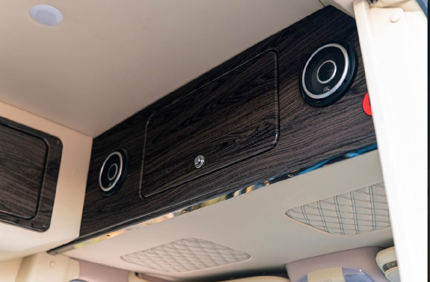 RV rental: Overhead dark wood-look cabinets, integrated speakers, and a ceiling light inside a modern vehicle.