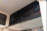 RV rental: Overhead dark wood-look cabinets, integrated speakers, and a ceiling light inside a modern vehicle.