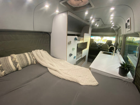 Inside a modern rv rental: comfy bed, fun bunk beds with climbing holds, and a sleek kitchen area.