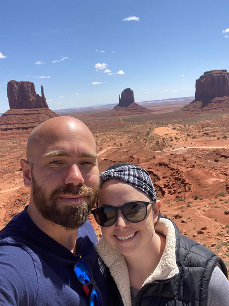 Smiling duo on an adventure amidst stunning desert buttes. Ideal for an RV rental getaway!