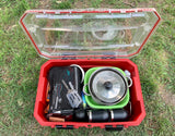 A red outdoor case open on grass, revealing neatly packed camping cooking gear: pots, utensils, and mugs. Ideal for your RV rental adventure!