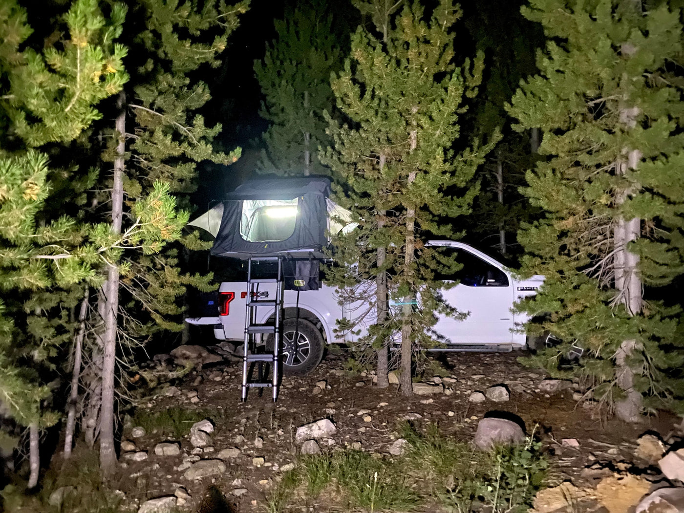 White pickup truck with a lit rooftop tent for night camping. An ideal RV rental for off-grid adventure. — photo 6