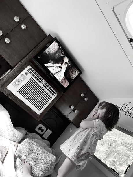Child looking out window inside a compact rv rental, featuring TV, AC, and comfy blankets.