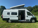 White camper van, ideal RV rental, with open side door, visible interior ladder, and extended pop-top on grass.