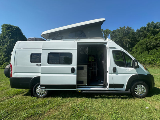 White camper van, ideal RV rental, with open side door, visible interior ladder, and extended pop-top on grass.