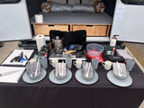 An RV rental's organized outdoor kitchen with a stove, coffee pot, cooking gear, and place settings for four.