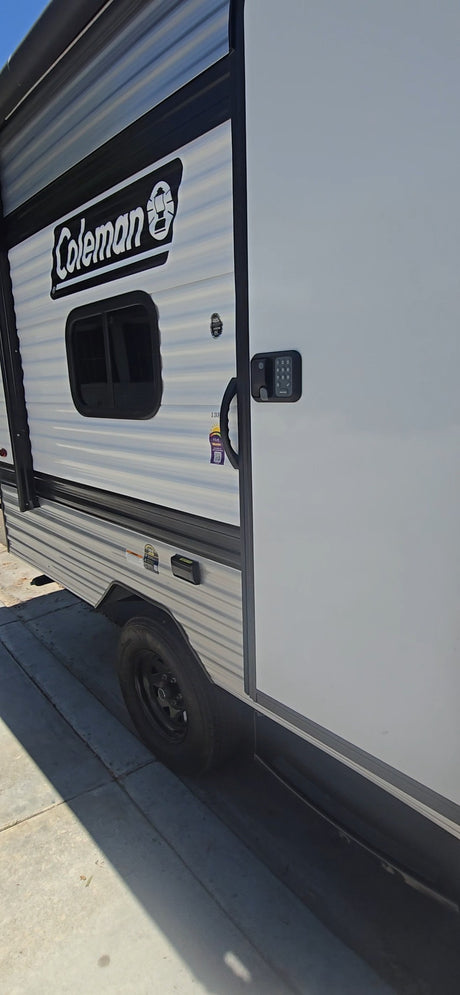 Side view of a white Coleman rv rental travel trailer, featuring a door with keypad lock, handle, and window.