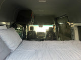 Inside an RV rental, a comfy bed fills the foreground, leading to the front cabin with seats and overhead storage.