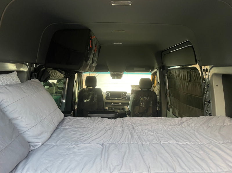 Inside an RV rental, a comfy bed fills the foreground, leading to the front cabin with seats and overhead storage. — photo 14