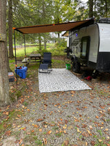 Relaxing rv rental campsite with a small travel trailer, extended awning, outdoor rug, chair, cooler, and picnic table.