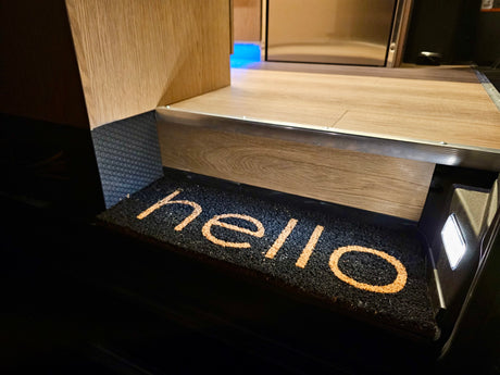 Welcome aboard! An inviting RV rental interior features a "hello" doormat illuminated by a step light.