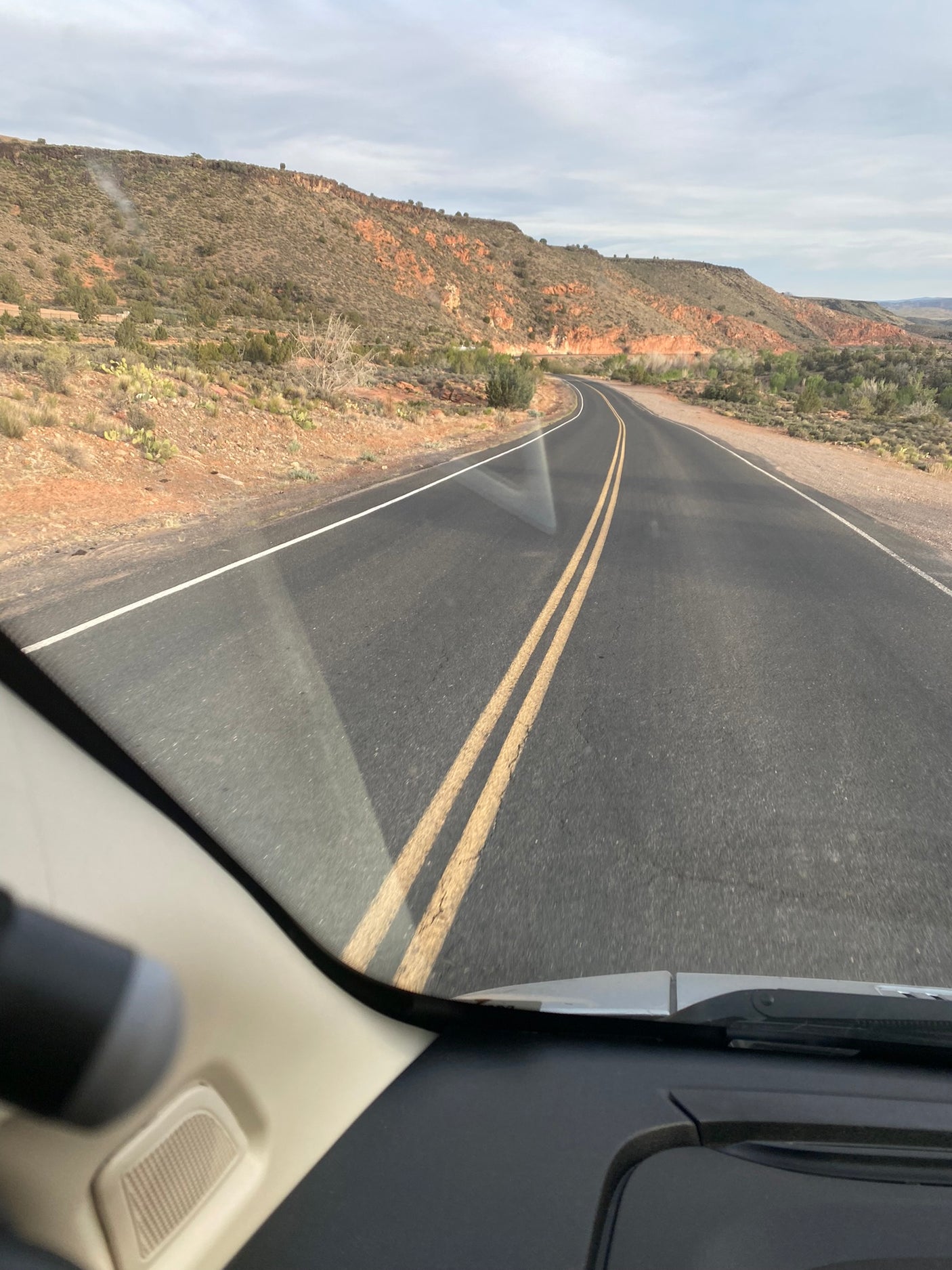 RV rental road trip: Winding desert road through arid mountains with sparse plants. View from inside the vehicle on an overcast day.