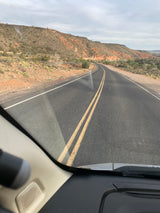 RV rental road trip: Winding desert road through arid mountains with sparse plants. View from inside the vehicle on an overcast day.