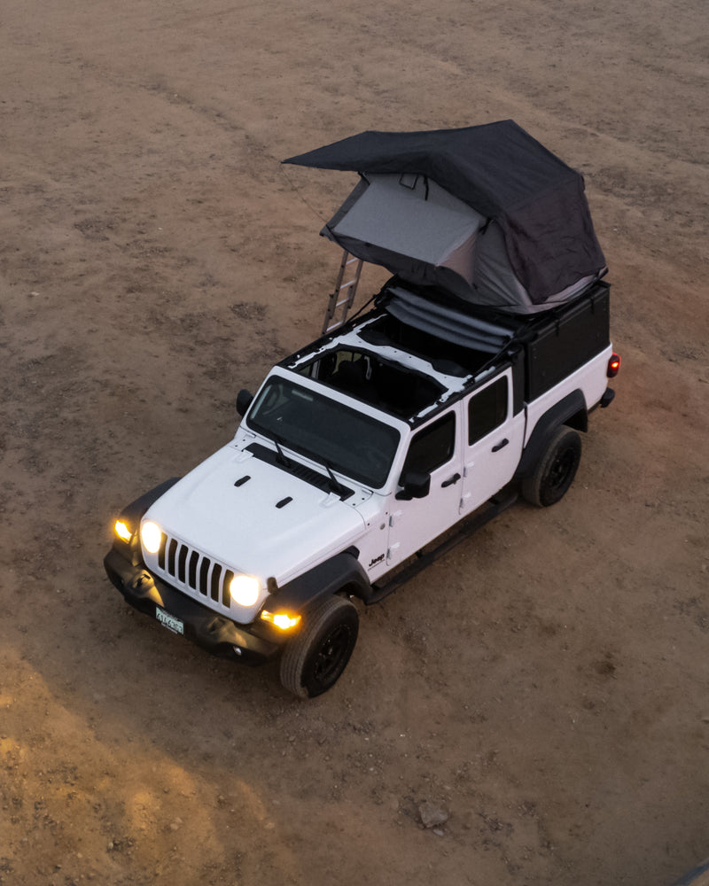 A white Jeep Gladiator with a deployed rooftop tent is parked on dirt. Ideal for an outdoor adventure or an RV rental for camping. — photo 11