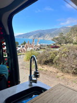 View out an RV's open door showing a sink, coastal mountains, and blue ocean. Perfect for your next RV rental journey.