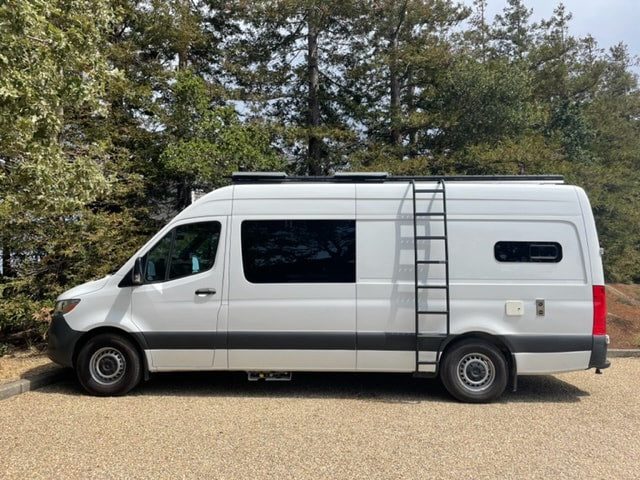 White converted camper van, an rv rental, with roof ladder, parked on gravel by trees. — photo 9