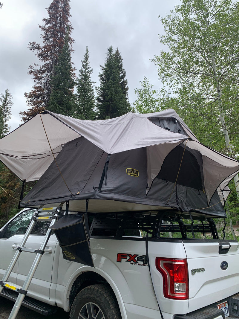A white F-150 FX4 with a grey rooftop tent set up in the woods. A rugged alternative to an RV rental for off-road camping. — photo 7