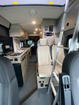 Interior of an RV rental, featuring a compact kitchenette, ladder to bunk, and comfortable seating. Ready for adventures!