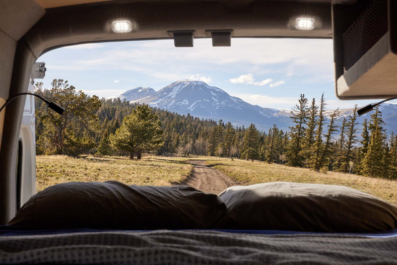  parked on a dirt road amidst scenic mountains and forests.|Wake up to stunning mountain views from your comfortable rv rental bed. Explore nature on your next adventure.|Titus Adventure Co. RV rental in a breathtaking desert canyon. Perfect for van life & exploring iconic red rock landscapes.|Inside an rv rental camper van: screen door open — photo 6