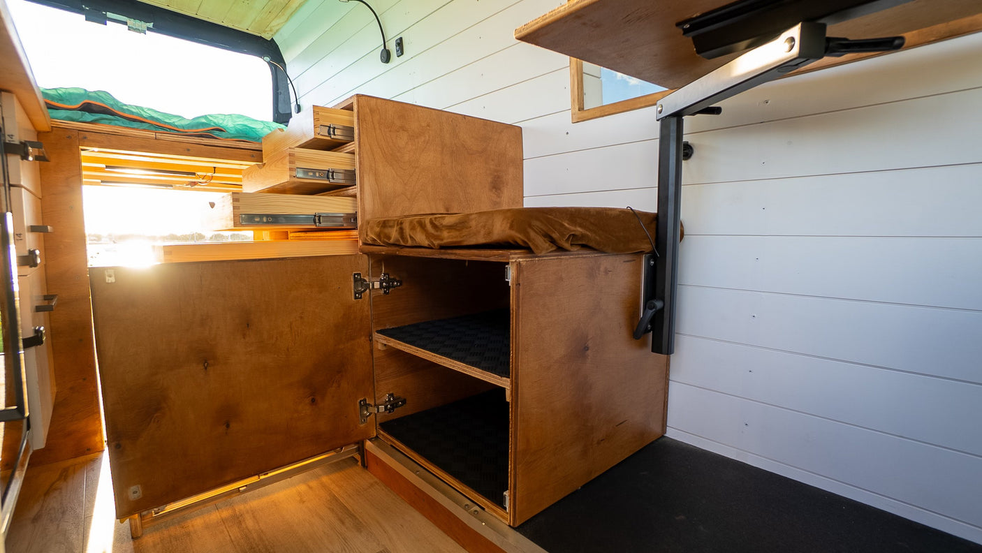 Bright RV rental interior: custom wooden storage, open drawers, bench, and cabinet for organized travel.