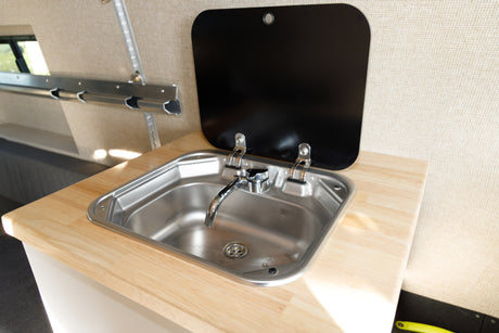 An open, compact stainless steel sink with a chrome faucet on a wood countertop inside an RV rental.