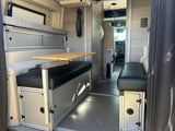 Spacious RV rental interior with a versatile table, cushioned benches, overhead bed, and hidden storage for comfortable travel.