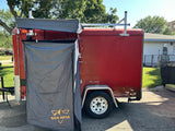 Red cargo trailer converted for RV rental use, featuring a deployable privacy tent and roof rack.