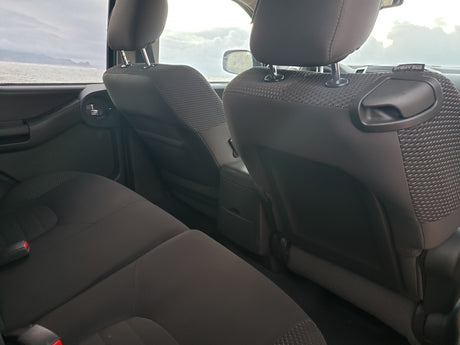 Interior of an RV rental: dark fabric back seats facing a window view of the ocean, distant mountains, and cloudy sky.