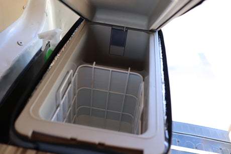 Inside an RV rental's portable cooler, featuring an open lid, interior storage basket, and a spray bottle nearby.
