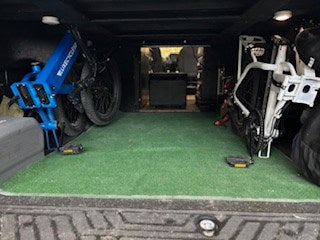 RV rental cargo bay: two folded electric bikes, blue & white, on green turf, ready for your next adventure trip.