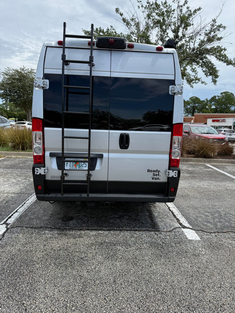 Rear view of a silver camper van, possibly an RV rental, with a ladder and "Ready. Set. Van." text in a parking lot.