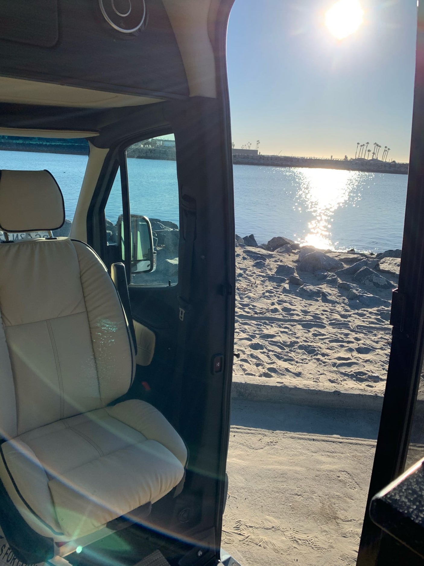 Inside an RV rental, a stunning beach view: sandy shore, sun-drenched water, and distant palm trees. Perfect for adventure.