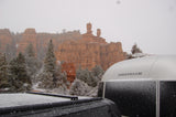 Snow falls on red rock formations, pine trees, and an Airstream rv rental.