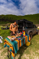 A man cooks outdoors from his overlanding vehicle, an ideal RV rental for scenic adventures. Fresh food prep.