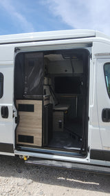 Inside an RV rental: a white camper van's interior, showcasing a compact kitchen & bed area. Perfect for van life.