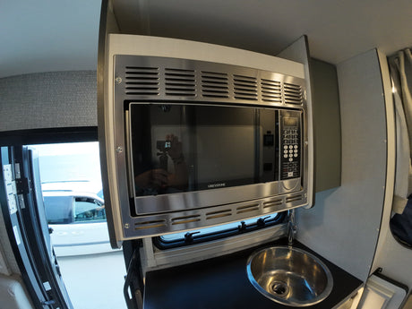 Compact rv rental kitchen: stainless Greystone microwave oven above a small sink. Outdoor view through open door.
