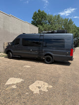 A dark gray Sanctuary camper van, equipped for adventures, stands as an ideal RV rental by a wall.
