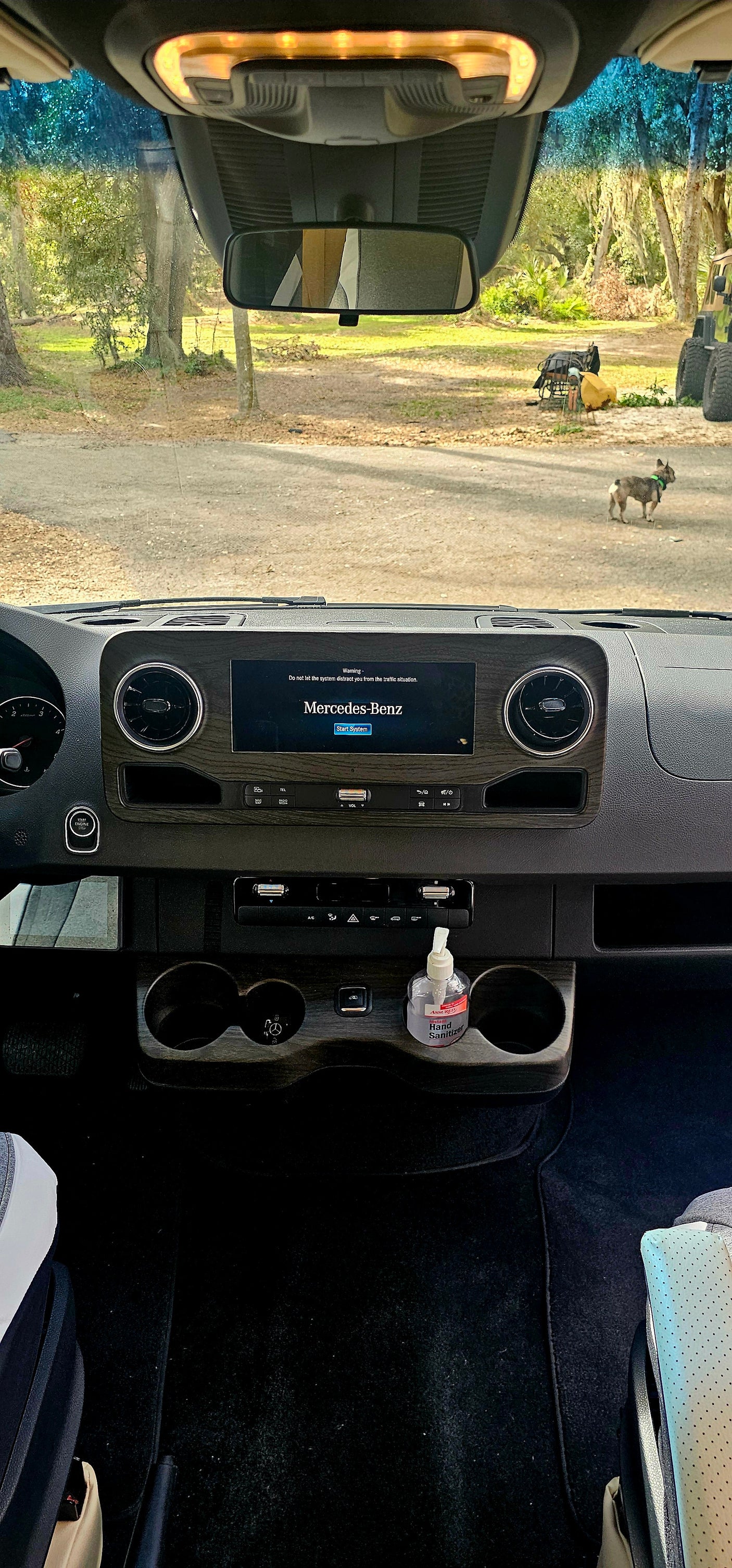 Inside an RV rental: Mercedes-Benz dashboard and infotainment screen (startup warning), hand sanitizer, plus a dog playing outside.