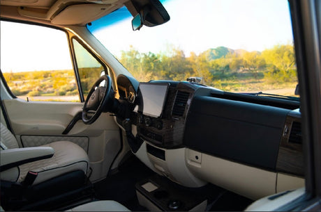 Inside a comfortable RV rental: driver's area with modern tech & plush seating, overlooking a vast desert landscape.