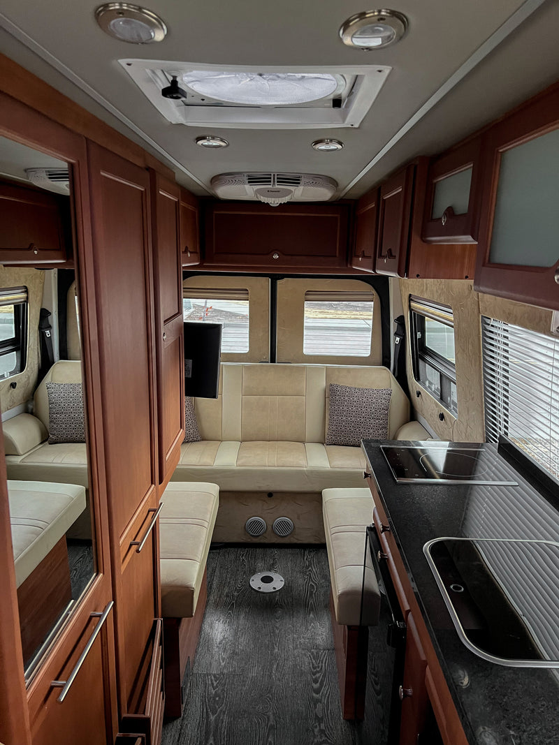 Interior view of an RV rental: light wood cabinets, beige seating, kitchen with black counters, & dark wood floor. — photo 11