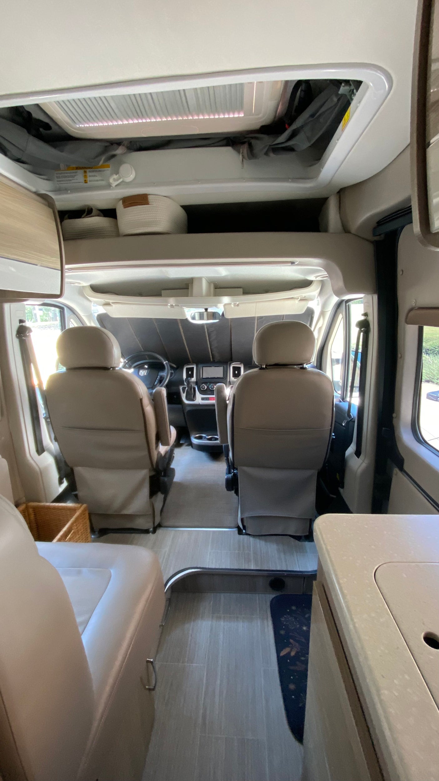 Spacious RV rental interior with light-colored seating, dashboard, overhead storage, and a kitchen counter visible.