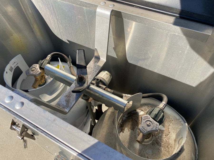 Two propane tanks with a regulator visible in a metal RV rental storage compartment.
