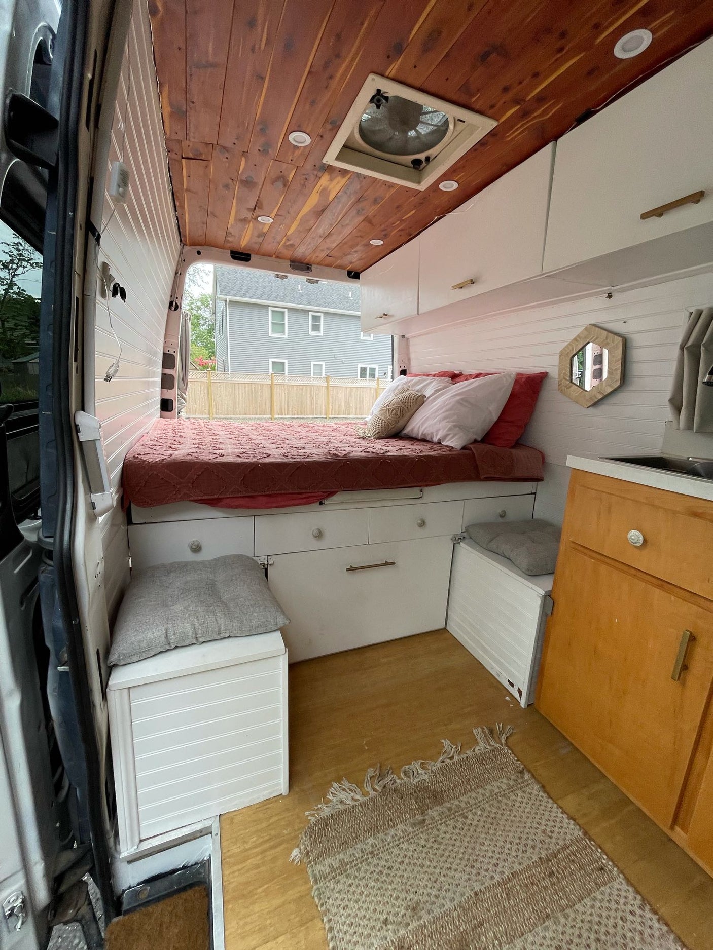 Cozy RV rental interior: bed with storage, overhead cabinets, wood ceiling, and a compact kitchen area.